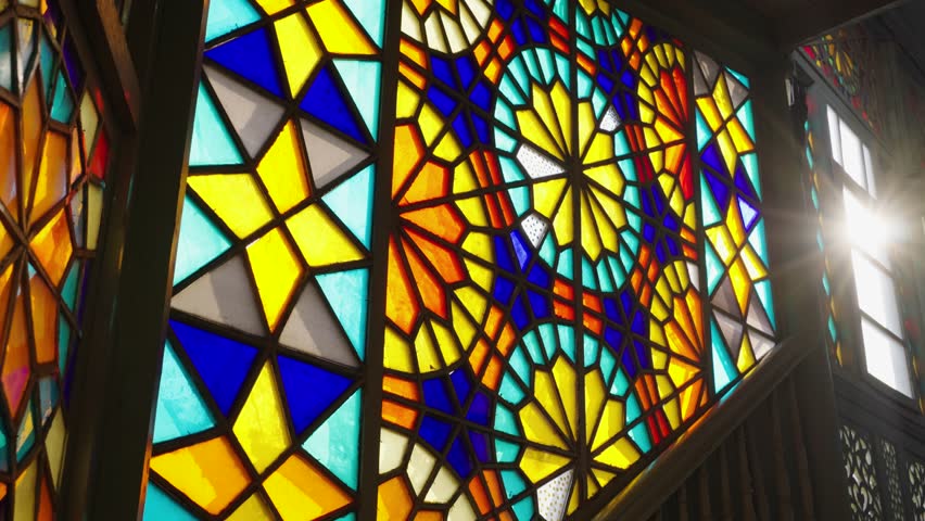 Multicolored stained glass vintage windows with patterns glow during the day, the camera slowly rises up the stairs with a ray of sun in the gap in a historic building or church, vintage front Royalty-Free Stock Footage #1103528193