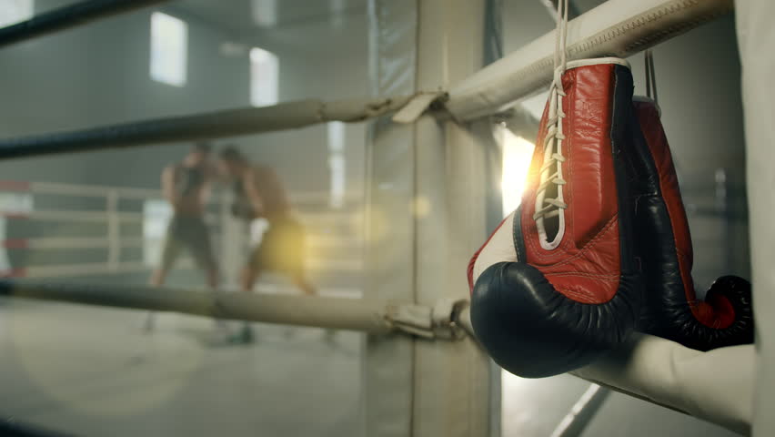 Blurred boxing fight. Two boxers throw punches at each other on the ring. Pair of red boxing gloves hang on the rope of white color boxing ring. High quality 4k footage Royalty-Free Stock Footage #1103528545
