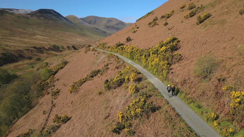 Hikers walking along hillside track on sunny day Coledale Beck in the English Lake District Cumbria