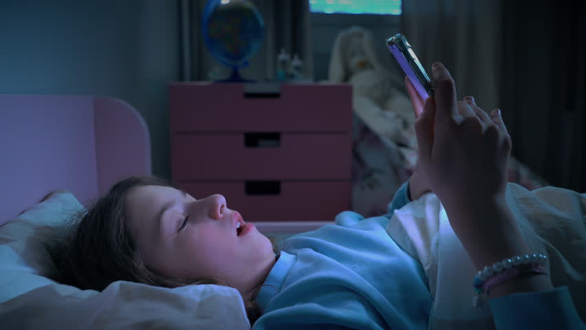Teen girl lying in bed at night using smartphone, scrolling social media and texting. Not healthy sleep. Insomnia and the harm of the smartphone before going to bed. Dependence on social networks