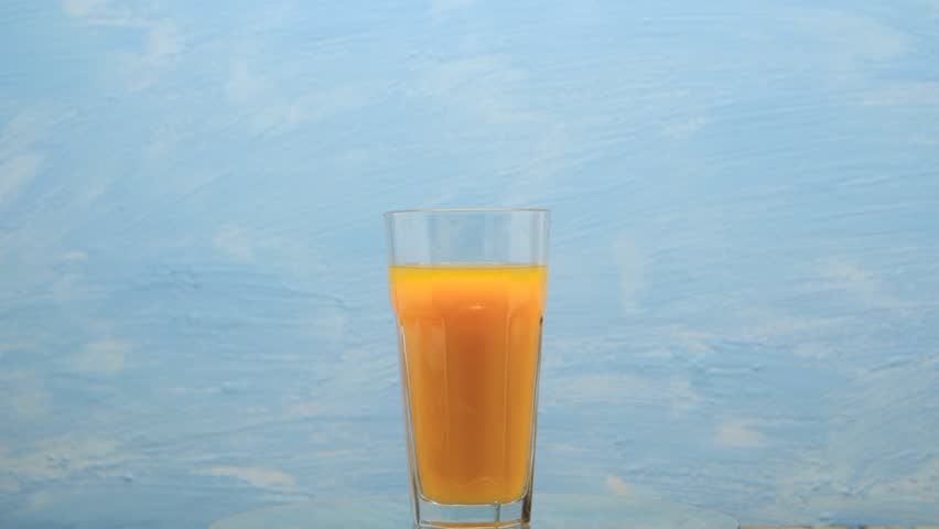 Rotation of orange juice in a glass. Cocktail with orange juice on a blue background. Royalty-Free Stock Footage #1103539785