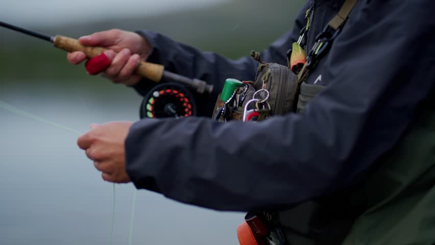Side close-up of equipment and hands of unrecognizable man fly fishing