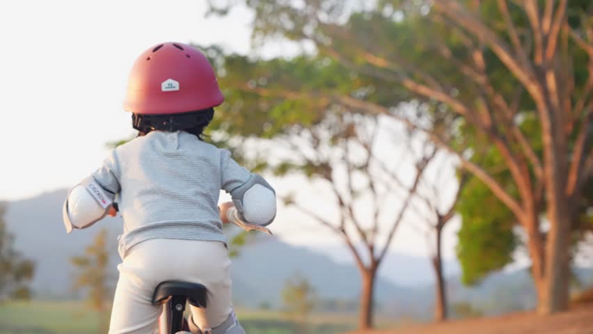 Behind shot of young playful child riding standing bike on the natural pathway, practicing how to ride a bike, outdoor activity for preschool age kid for mind skills muscles and bones development. Royalty-Free Stock Footage #1103542379