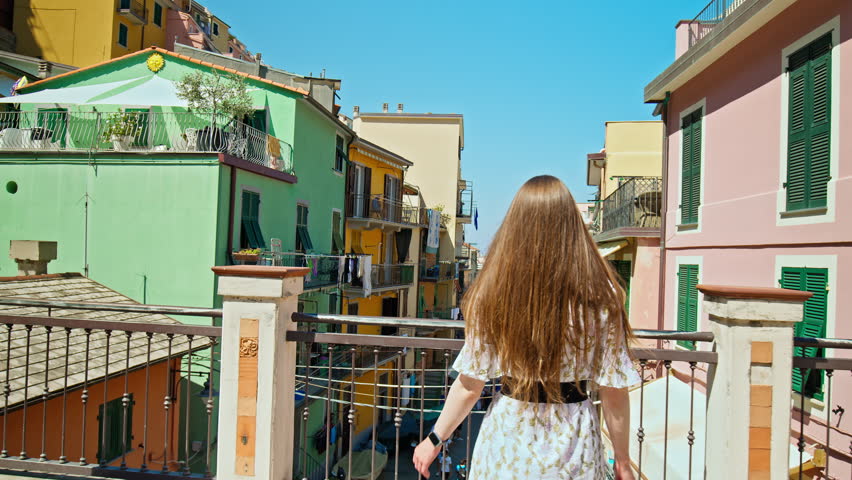 Young Tourist woman exploring European town, walking in Riomaggiore, Italian Riviera. The most southern village of the five Cinque Terre with a small beach and a wharf framed by colorful tower houses. Royalty-Free Stock Footage #1103542691