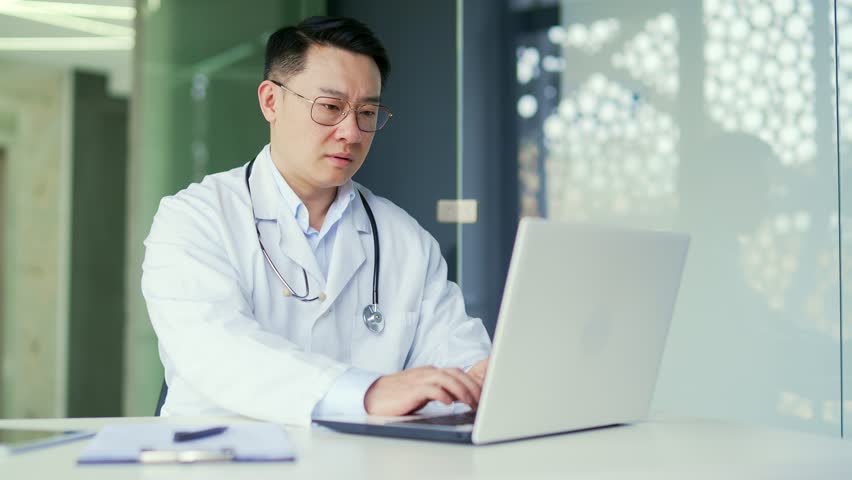 Overworked asian doctor suffering from eyestrain working on laptop while sitting in workplace in office in hospital clinic. A tired medical worker physician takes off his glasses, massages his temples Royalty-Free Stock Footage #1103553889