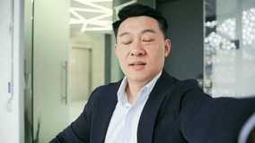 POV Webcam view. Close up of an asian businessman talking on a video call using a smartphone at a workplace in a modern office. An entrepreneur in a formal suit communicates remotely, talks online