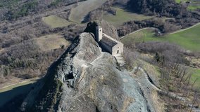 Aerial footage of Pietra Perduca, volcanic rock, church set at top stone immersed in countryside landscape, cultivated land in Val Trebbia Bobbio, Emilia Romagna, Italy