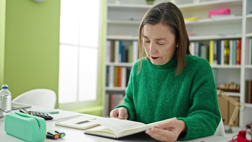 Mature hispanic woman with grey hair sitting reading book at library