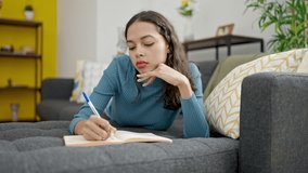 Young beautiful hispanic woman writing on notebook lying on sofa at home - Powered by Shutterstock - Get 15% off with code: PIKWIZARD15