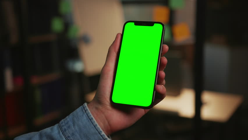 Footage of modern smartphone in male hands isolated on blurred background of office in evening. Close-up shot of unrecognizable man using gadget with green screen. Chroma key concept. Indoors Royalty-Free Stock Footage #1103559319