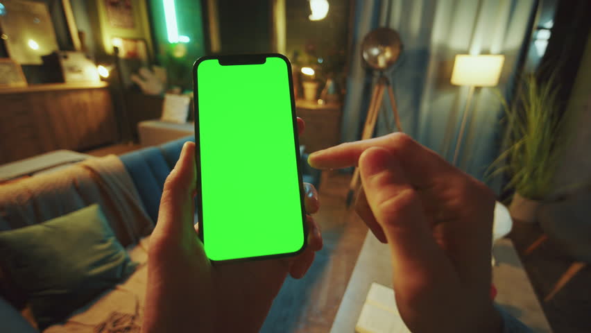Close up man holds a scrolling phone with a vertical green screen in a dark room. Device. Smartphone. Social media