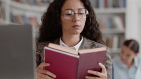 Self education time. Young smart woman student wearing eyeglasses reading book in college library, studying topic or making research for homework project, tracking shot, slow motion - Powered by Shutterstock - Get 15% off with code: PIKWIZARD15