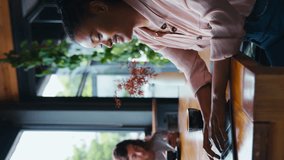 Vertical video of smiling young businesswoman with coffee sitting in informal seating area of office working on laptop with colleague in background - shot in slow motion