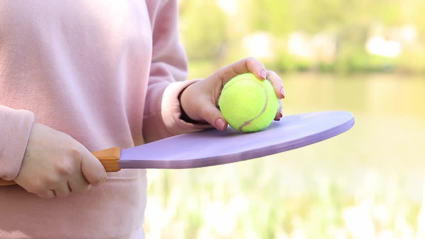 The player is holding a tennis racket. Waiting game in nature. Wooden tennis racket and ball in hand. Outdoor games near the lake