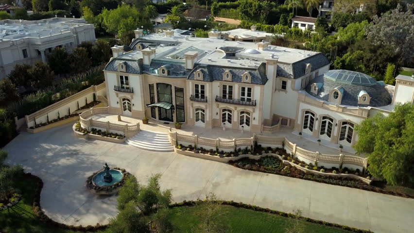Aerial Panning Shot Of Mansion With Fountain By Plants On Sunny Day, Drone Flying Over Residential Structures - Beverly Hills, California