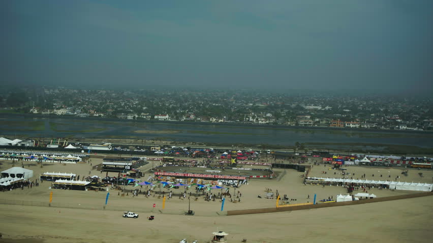 Aerial Panning Shot Of People At Event Venue Near Houses In Suburb, Drone Flying Over Beach Against Sky - Huntington Beach, California