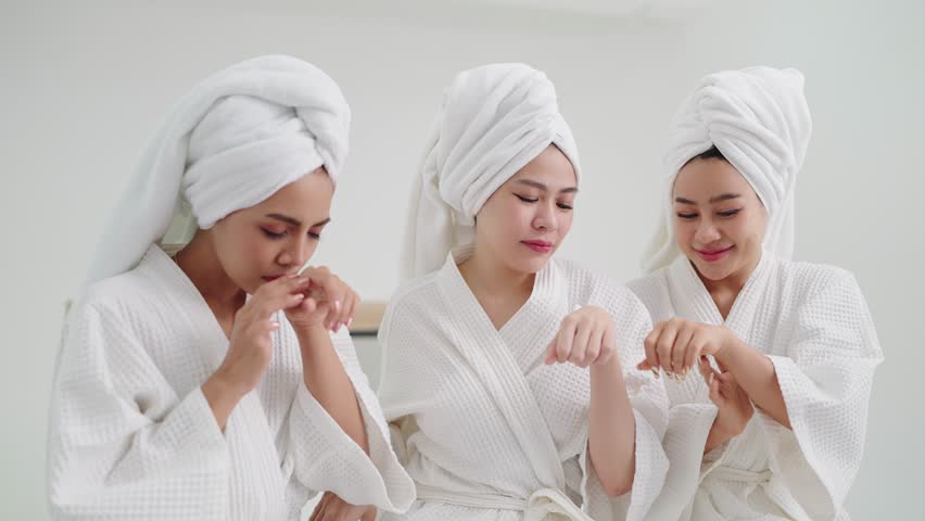 Group of young beautiful Asian woman in white bathrobe enjoy applies moisturizing cream to skin feeling fragrant smell. Skin care concepts Royalty-Free Stock Footage #1103573635