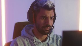 Attractive Middle East man putting on headphone playing computer SPF or MMORPG game upset looking at screen focus on match disappointed lose defeated. Unhappy young male sit in RGB gaming room