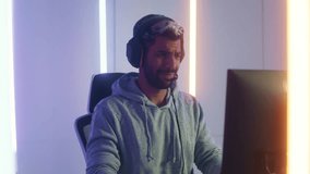 Attractive Middle East man gamer on headphone playing computer SPF or MMORPG game upset looking at screen focus on match disappointed lose defeated. Unhappy young male sit in RGB gaming room