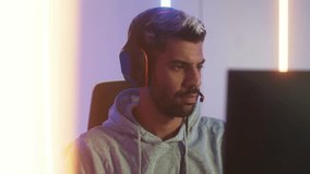 Attractive Middle East man putting on headphone playing computer SPF or MMORPG serious looking at screen focus on online game. Handsome young male gamer wearing headset sit in RGB gaming room