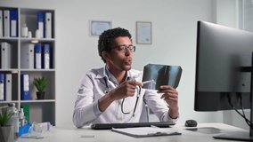 accepting patients online, young black doctor with help of video call and shows x-ray while sitting in a Melecian office