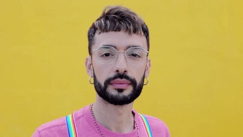 Smiling portrait of young cheerful bearded gay man looking at camera over yellow background. LGTBQ people concept Video de stock
