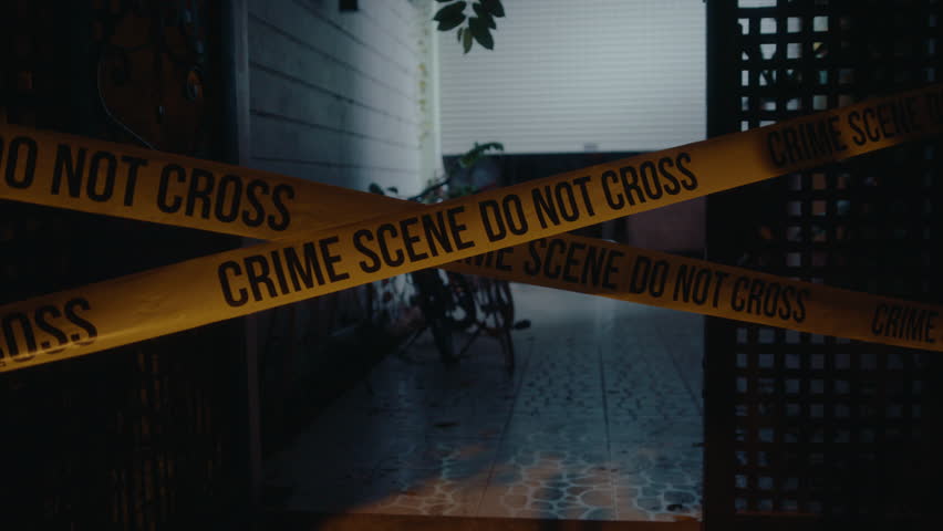 Yellow police tape with Crime Scene Do Not Cross sign isolating entrance of dark house at night, illuminated by police car lights. Medium no people shot