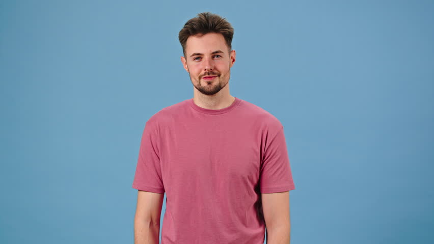 Handsome man admires own appearance smiling contentedly. Narcissistic male winks and touches face. Person straightens hair and T-shirt on blue background Royalty-Free Stock Footage #1103591149