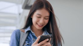 Young asian woman smiling using mobile smart phone outdoor. Happy female tourist wearing jeans jacket and holding smartphone at public