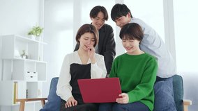 A casual group of four Asian men and women looking at a laptop together.