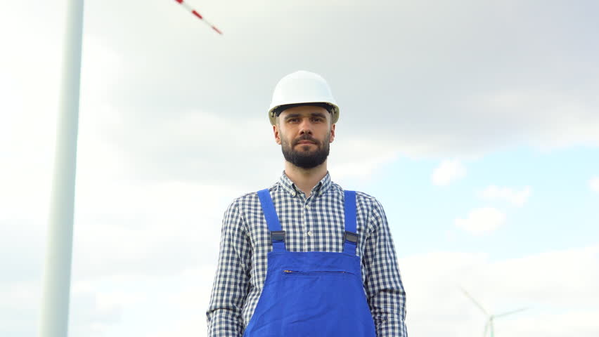 Portrait of worker in uniform at wind farm. Clean renewable energy technologies. Wind power plants