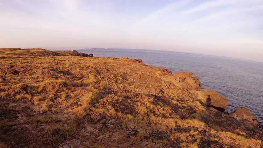 horizontal pane look out view of coastal scenery at Dung Lung Cliff with dry brown bush grass in front and horizon ocean line with calm sea water at back with clouds blue sky during sunset afternoon