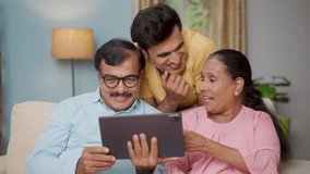 Indian Senior parents with adult son watching digital tablet by talking together at home - concept of communication, parenthood and interaction - Powered by Shutterstock - Get 15% off with code: PIKWIZARD15