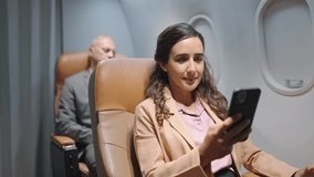 Hispanic latino businesswoman using smartphone video call with partnership while sitting in seat on airplane and drinking water. Travel and business concept