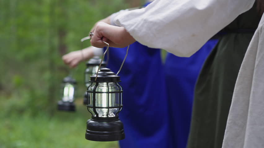 Group of women wearing medieval dresses carries lanterns walking through wild wood close backside view. Mystical ritual in nature. Role playing at quest Royalty-Free Stock Footage #1103613031
