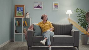 Relaxed mature lady listens to music with headphones while little girl jumps with hula hoop at home. Grandmother babysits granddaughter in living room - Powered by Shutterstock - Get 15% off with code: PIKWIZARD15