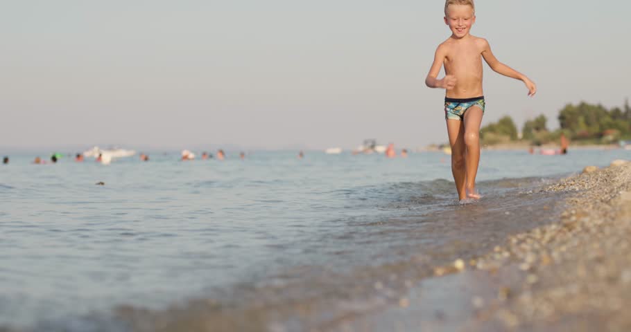Kid running on a beach. Abstract slow motion male feet on pebbles and sand.