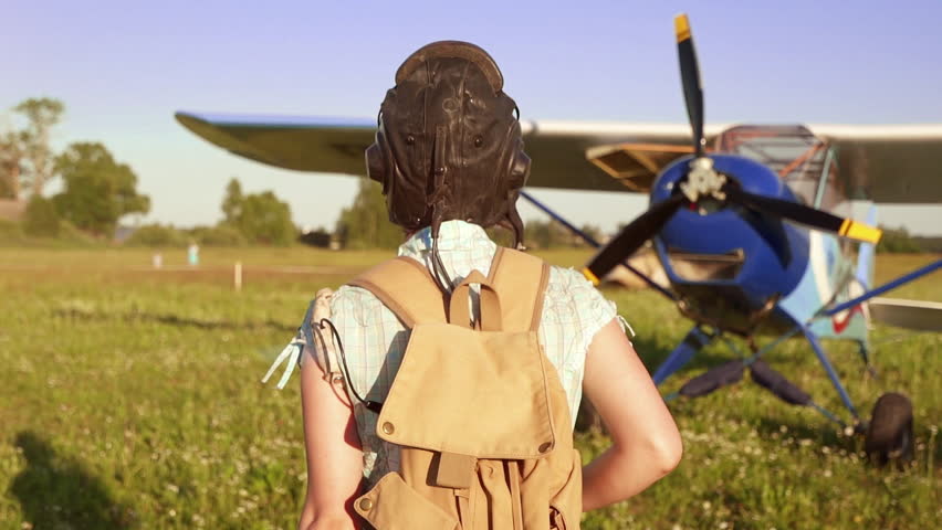 Young adventurous woman pilot walking to old airplane at summer sunset. Freedom and feminism concept. Breathtaking adventure in the air. Proffesional captain girl preparing for flight and skydiving