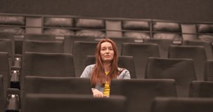 Young caucasian woman clapping her hands in an empty cinema hall. Beginning of the movie.