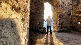 Wide angle 4K video shot of warm clothed tourist woman enjoying the sunset sun light in medieval Slovakian castle ruins during autumn nature walk. Stary Hrad Strecno, Zilina, Slovakia.