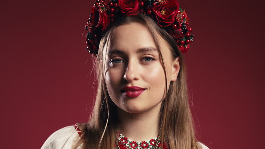 Charming ukrainian woman in traditional outfit, wreath on red studio background.