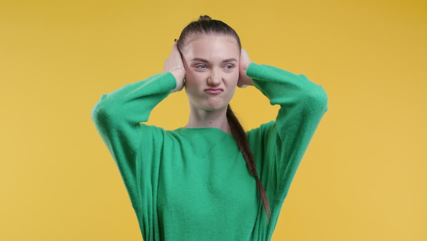 Irritated young woman with covered ears ignoring on yellow background.