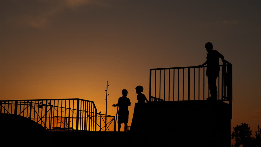 Children happiness during roller skating. Children silhouettes driving and relaxing on roller skates platform against evening sky in summer. Royalty-Free Stock Footage #1103635431