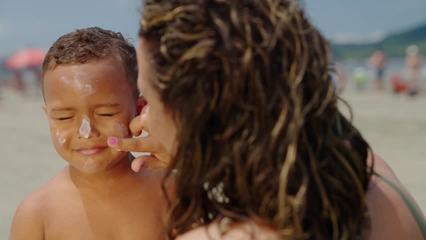 mother applying sunblock lotion on sons skin for sun protection little boy getting ready to swim on the beach with mom using sunscreen caring for childs health on sunny day 
 Royalty-Free Stock Footage #1103635527