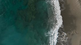 Cinematic Top down abstract aerial view of ocean waves crashing on rocky shoreline Static vertical aerial footage drone video top view stormy beach graphic art shadows on sand.