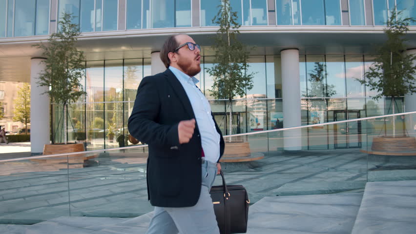 Overweight businessman dance commuting to work. Happy fat entrepreneur walk outside business center and dance. Realtime.  Royalty-Free Stock Footage #1103645431