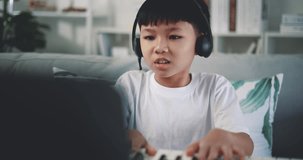 Handheld shot, Creative asian boy wearing headphone with artistic skills taking music lessons online during a video call and playing the piano at home. Music, hobby and lifestyle concepts.