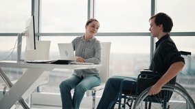 Young male office worker in a wheelchair talking to female colleague while showing her ideas using laptop in co-working space. Disability and handicap concept. Office modern people at work. - Powered by Shutterstock - Get 15% off with code: PIKWIZARD15