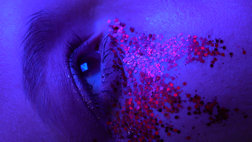 Close-up view of female face with shiny stage makeup with sparkles. Beauty night shot of woman eye illuminated blue purple color neon lighting. Selective focus. Vertical handheld video. Part of series Royalty-Free Stock Footage #1103647997