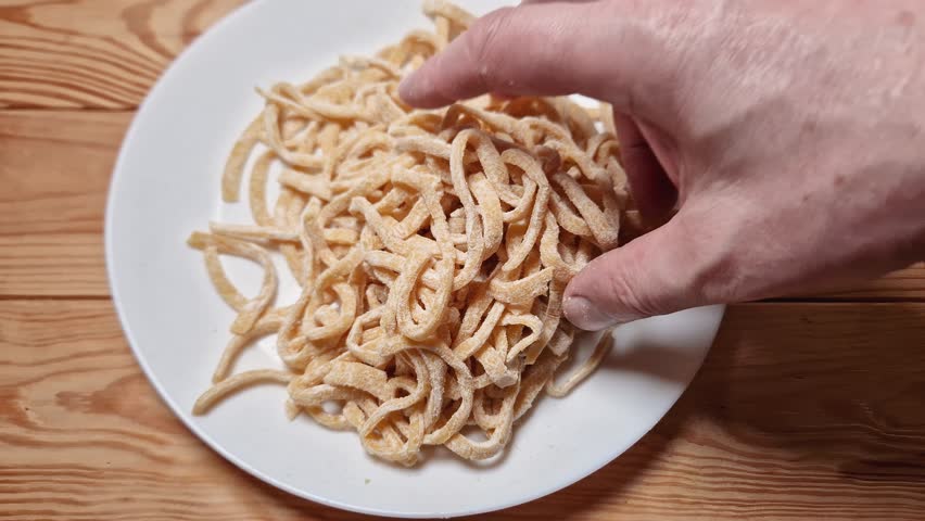Raw freshly prepared homemade egg noodles in the shape of the long strips on a white dish on rustic table
